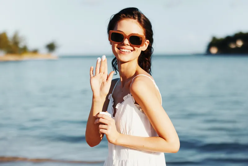 Smiling woman in sunglasses waving with blue sea background, summer dress, cheerful mood, sunny day, vacation atmosphere