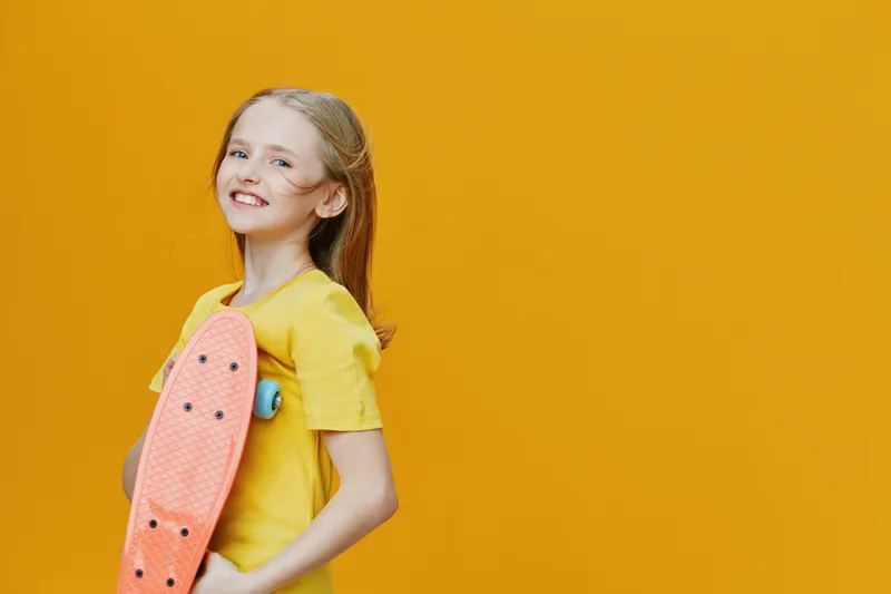 Cheerful girl in yellow t shirt holding a skateboard against a vibrant yellow background, embodying fun, youth, and active lifestyle Perfect for sports and recreational themes