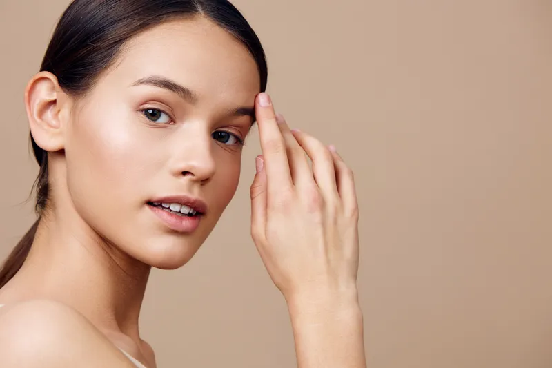Natural beauty portrait of a young woman with clear skin against a neutral background, showcasing a fresh and minimalistic aesthetic that emphasizes healthy skincare