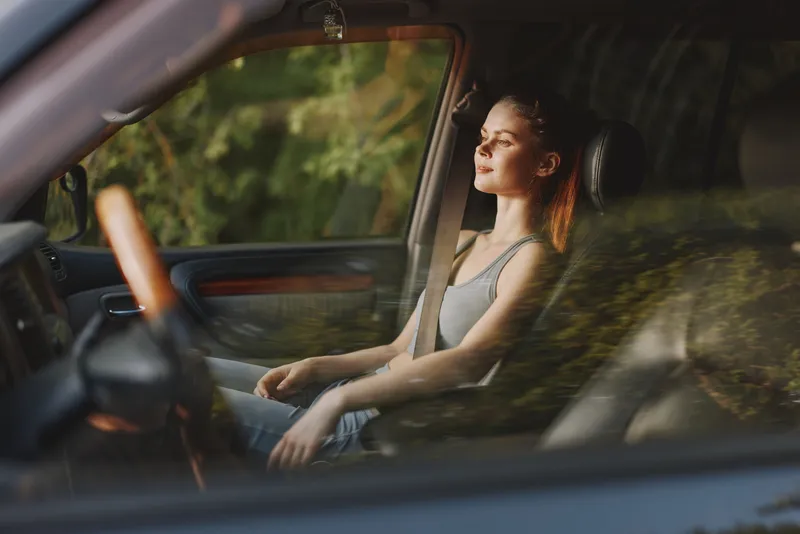 Relaxed young woman enjoying the serene outdoor scenery while sitting in a car, embodying tranquility and peace with a soft sunlight glow