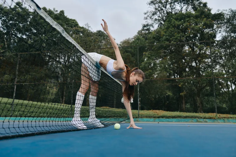 Female tennis player reaching for a ball on the court, showcasing athleticism and concentration in a natural outdoor setting with greenery