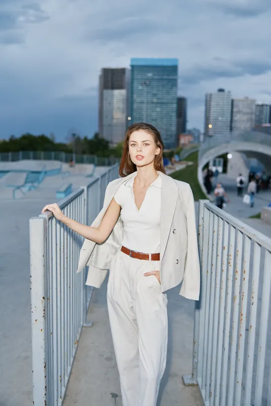 confident woman in white business outfit standing on urban bridge with modern cityscape background evening light business woman fashion