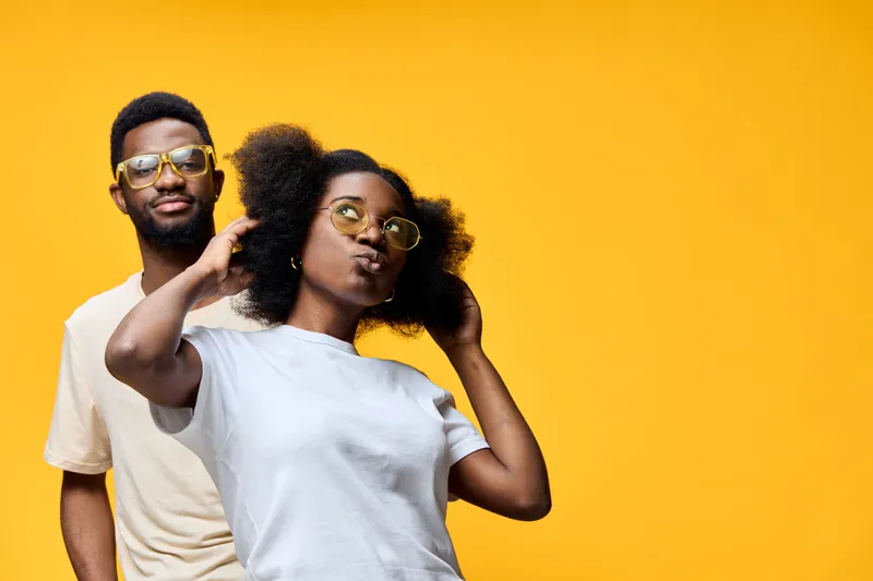 Young African couple wearing sunglasses against a bright yellow background, showcasing stylish fashion and playful emotions, ideal for vibrant lifestyle imagery