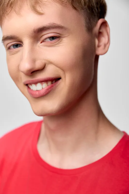 Smiling young male in a red shirt, closeup shot with a bright clean background, casual mood, upbeat expression, studio lighting highlighting a cheerful appearance today
