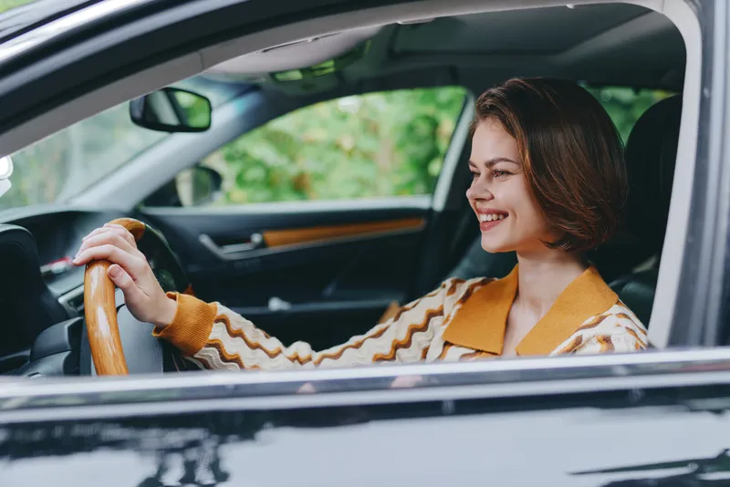 Cheerful woman driving a car, smiling and focused, holding the steering wheel with both hands, capturing a confident, relaxed travel moment.