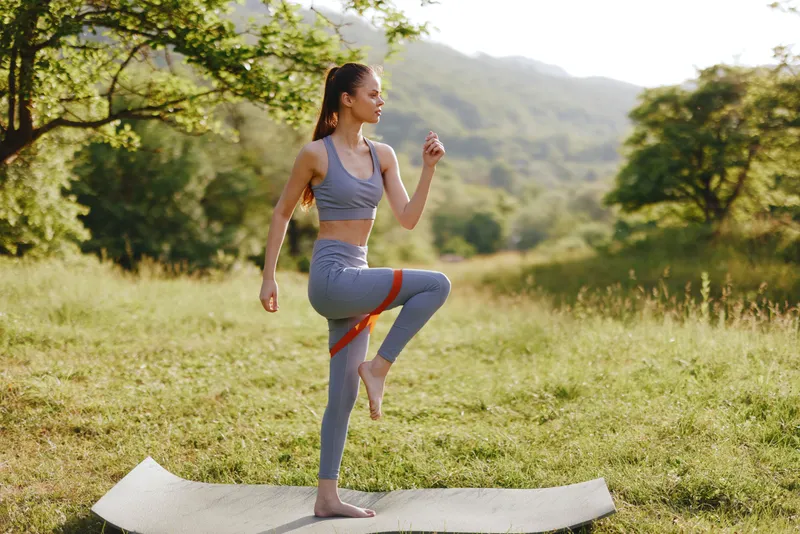 A young woman practicing yoga outdoors in a peaceful green environment, wearing gray sportswear, promoting fitness and well being during a sunny day