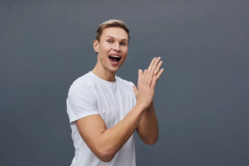 Smiling young man with enthusiastic expression wear casual white t-shirt isolated on plain gray background studio portrait. People lifestyle concept