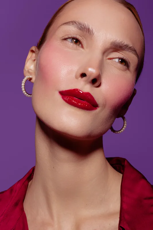 Close-up portrait of a woman with red lipstick and pearl earrings on purple background. Fashion makeup and beauty concept with soft lighting and elegant expression.