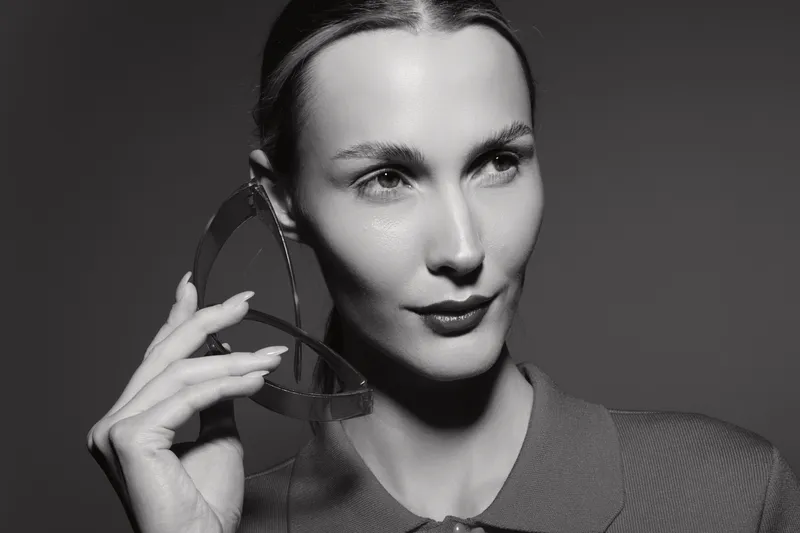 Portrait of a fair skinned Caucasian woman with slicked hair holding eyeglasses near her face in black and white.