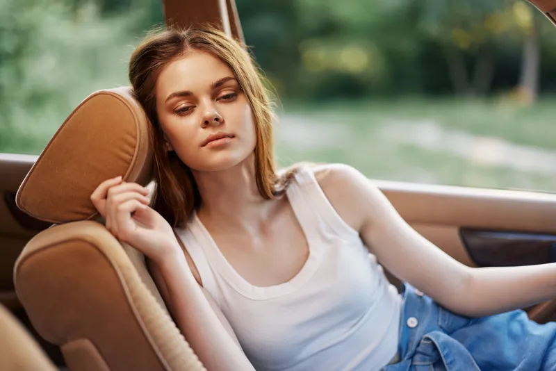 Tranquil young woman relaxing in a cozy car interior, enjoying a serene moment in nature, dressed casually in a tank top and denim shorts.