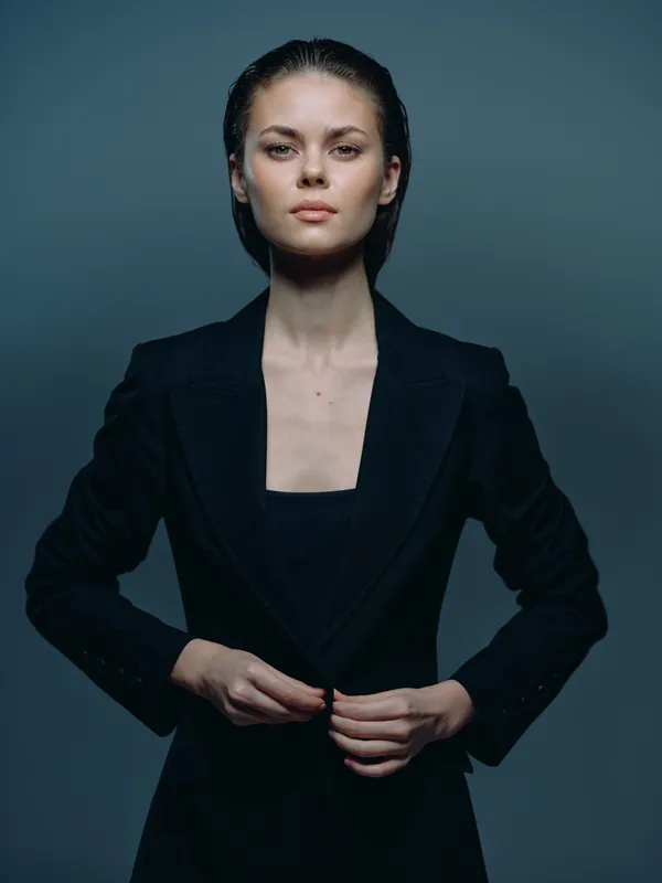 Confident woman in black business suit standing against dark background with serious expression and elegant posture