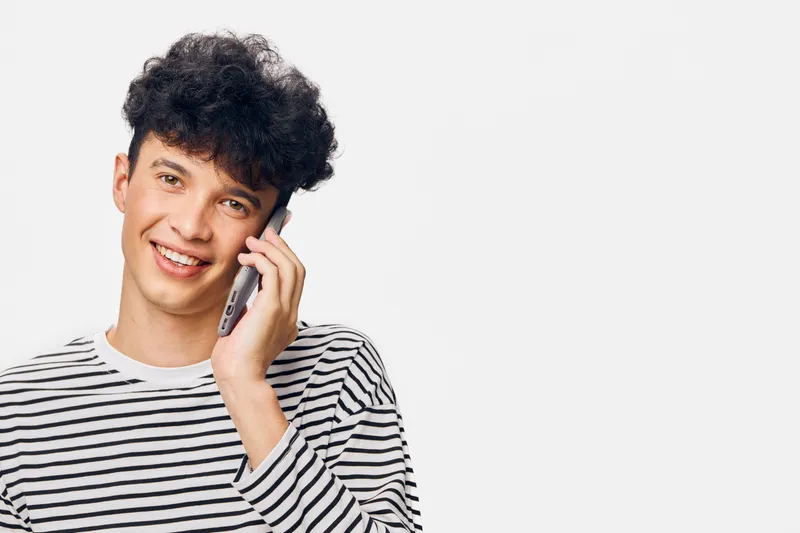 young man talking on the phone smiling, casual striped shirt, happy expression, isolated white background, positive communication moment