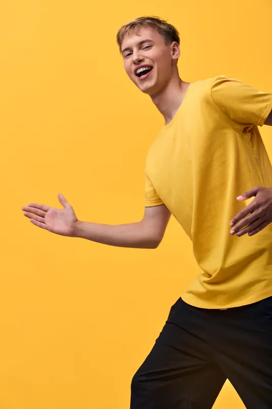 Joyful man in a yellow shirt moves with energy and a bright smile against a vivid yellow backdrop, capturing dynamic motion, casual fashion, and carefree mood.