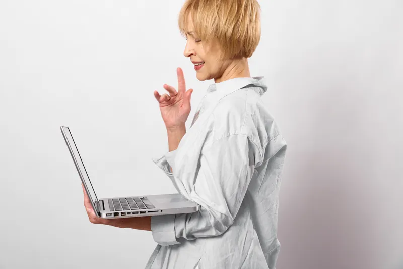 Woman laptop profile smile gesture talking communication learning, young blonde woman in studio with laptop, smiling and gesturing during conversation, white background