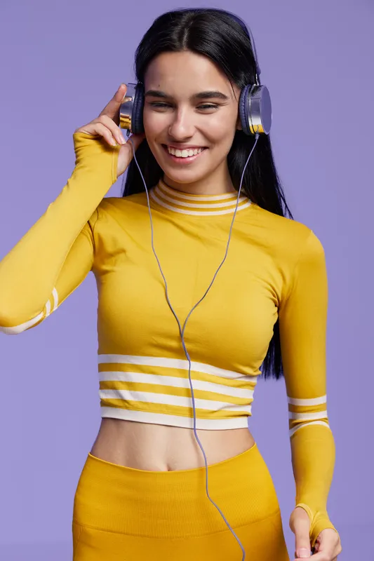 woman sport fitness wearing yellow activewear and headphones, smiling and enjoying music with purple background, healthy young adult, positive energy, vibrant mood