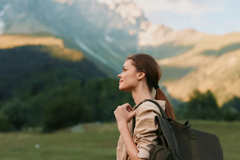 Young woman with backpack exploring a mountainous landscape, enjoying fresh air and scenic views, capturing a moment of outdoor life and freedom in nature.