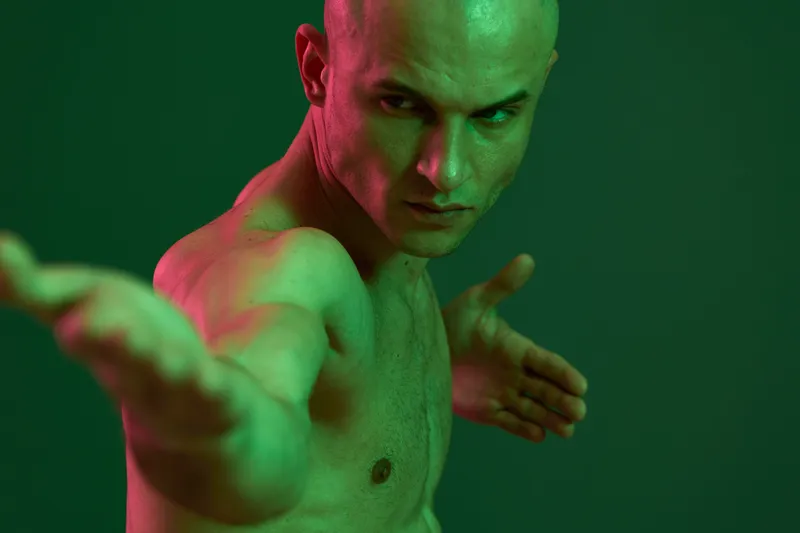 Artistic portrait of a muscular man showcasing strength and confidence against a dramatic green background. The image explores themes of power and determination.