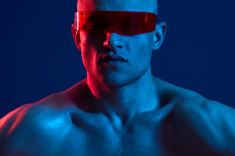 Strong man wearing futuristic red sunglasses with colorful lighting in a dynamic pose, showcasing modern style and confidence. Ideal for fashion and fitness themes.
