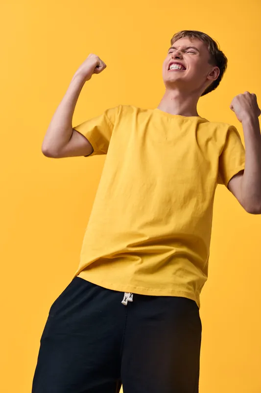 Boy in a bright yellow t shirt celebrates with clenched fists, energy and joy against a vivid yellow backdrop, conveying excitement, achievement and a positive mood for youth lifestyle visuals