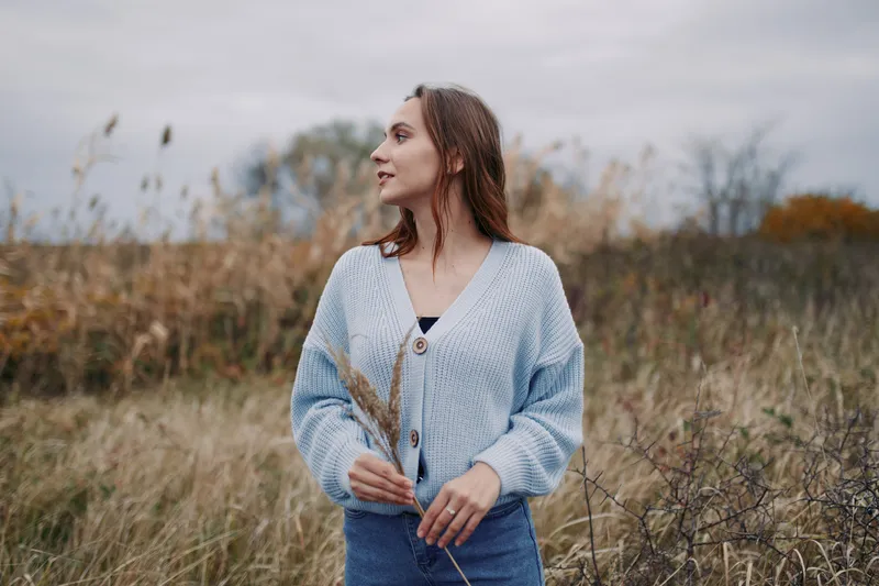A candid portrait of a young woman standing in a windswept field, conveying natural gestures and subtle emotion with authenticity and reliable documentary style, soft autumn light.
