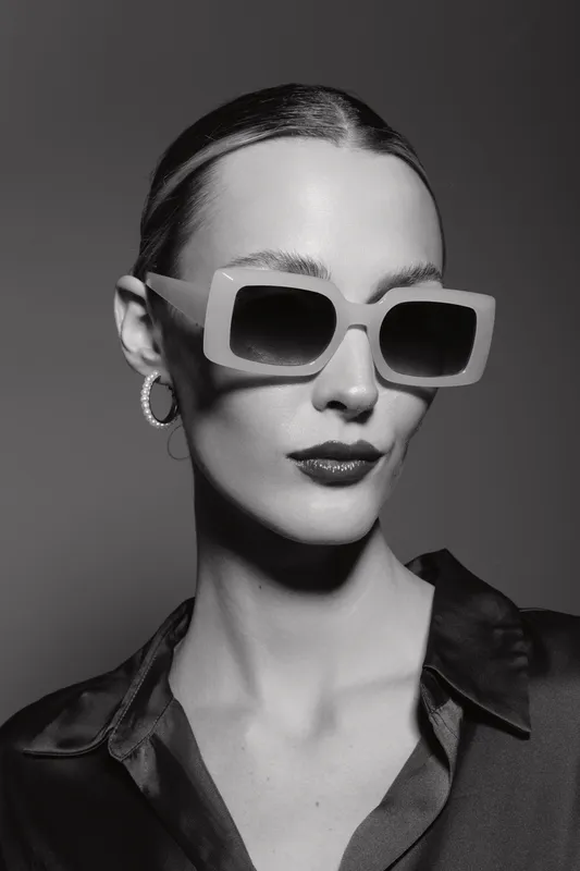 Stylish caucasian woman with pale skin wearing oversized sunglasses and hoop earrings. Black and white portrait with dramatic lighting and fashion concept.