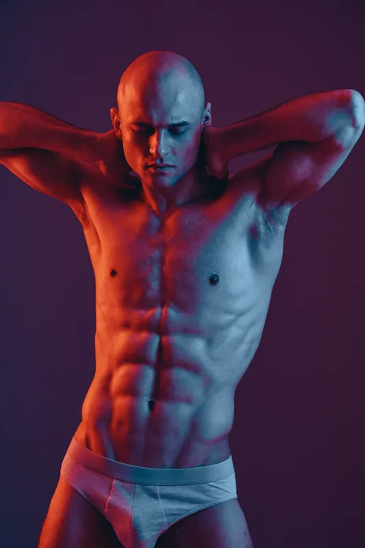 Muscular man posing confidently in a dramatic light, showcasing strength and determination with a modern artistic approach to fitness and health aesthetics.