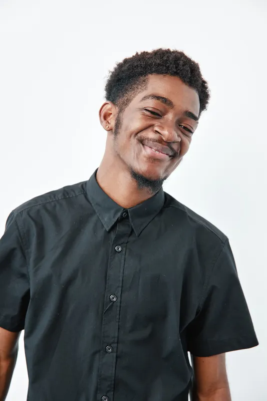 Young black man with dark skin and short curly hair wearing black shirt smiling confidently on white background. Portrait of African ethnicity male with casual style.