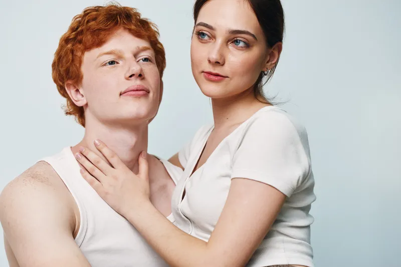 Couple, young man and woman in casual clothes looking thoughtful and close to each other with gentle touch in studio with plain background and natural light, love and connection.