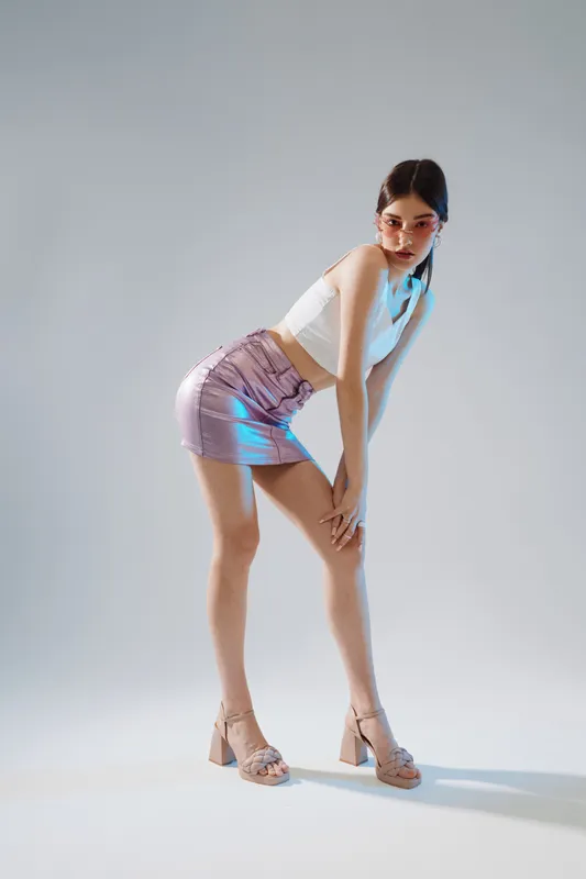 Young woman in a shiny purple skirt and white top poses confidently in studio lighting. Concept of beauty, fashion, and modern style with a minimalist background.