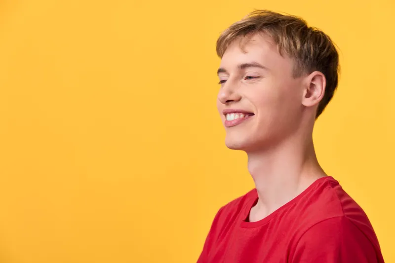 Smiling young man in a red shirt against a vivid yellow background, exuding happiness, relaxed confidence and approachable energy in a clean studio setting and branding