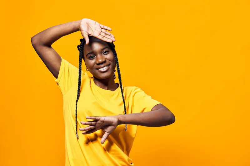 Happy young woman with braids wearing a yellow t shirt against a bright yellow background, expressing joy and positivity, perfect for seasonal themes