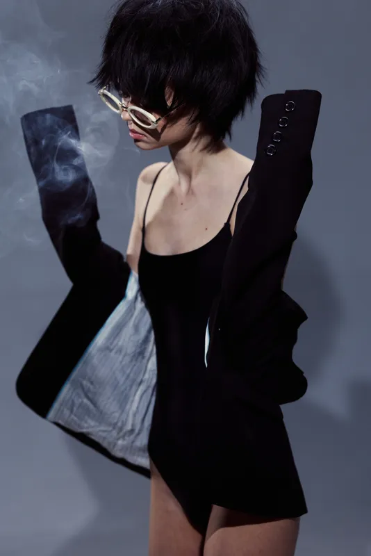stylish woman wearing black blazer with exposed shoulder and sunglasses in modern fashion pose