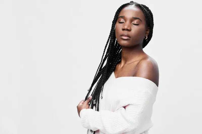 Young woman with braided hair in a white sweater, serene expression, emphasizing confidence and style against a minimalist white background