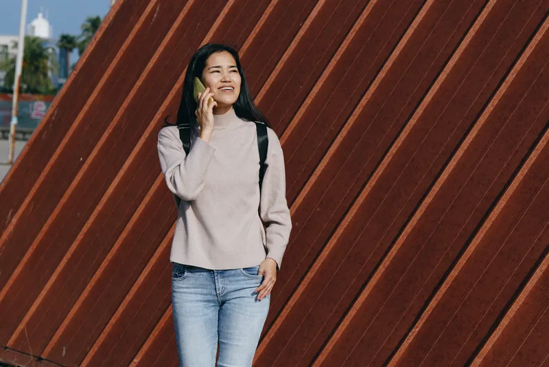 Woman talking on phone beside a diagonal wooden wall, casual outdoor setting, urban lifestyle and modern fashion emphasizing communication and confidence in a candid everyday moment