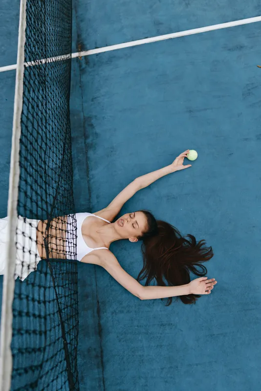 Female tennis player celebrating success with joyful expression on a blue court, wearing a sports top and shorts, conveying athleticism and dedication in a dynamic sports setting