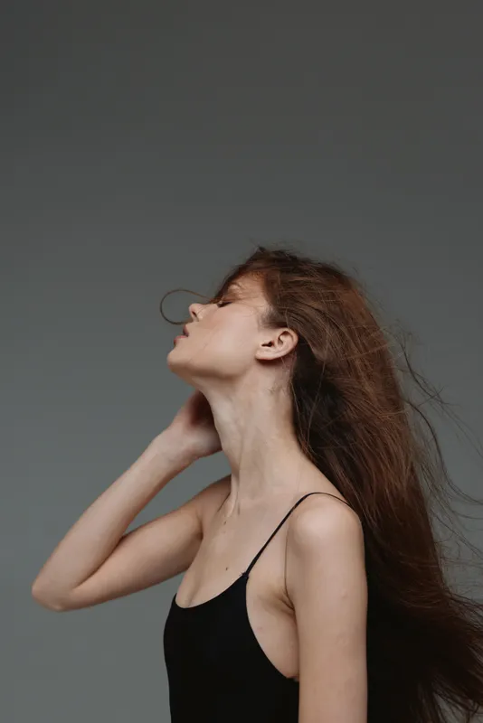 Profile of young woman with long hair in black top posing on gray background, elegant and contemplative mood.