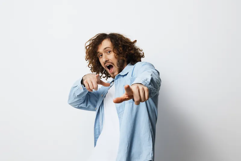 Young man with curly hair dressed in a light blue shirt, expressing joy and enthusiasm against a simple white background Modern and vibrant style, ideal for youth related themes