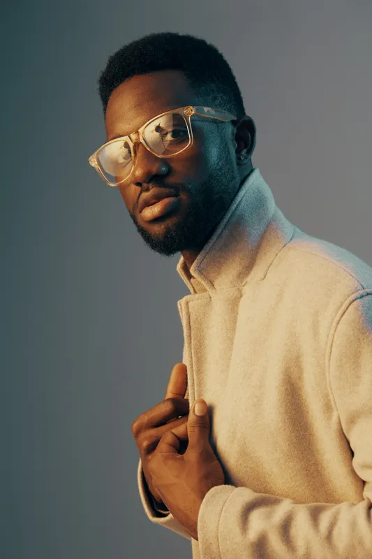 Stylish young man with glasses in a soft pastel colored coat, exuding confidence and sophistication against a minimalistic background