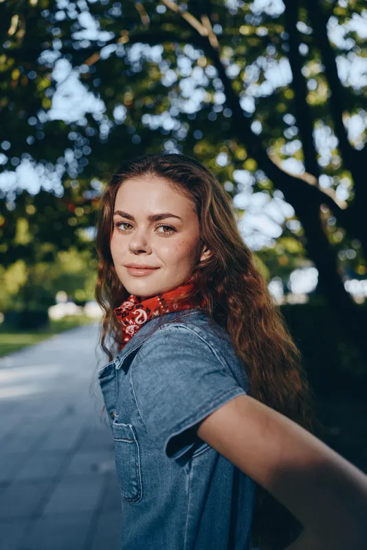 lifestyle woman in modern boho-western denim street style with film color tones, smiling confidently outdoors under trees during golden hour lighting