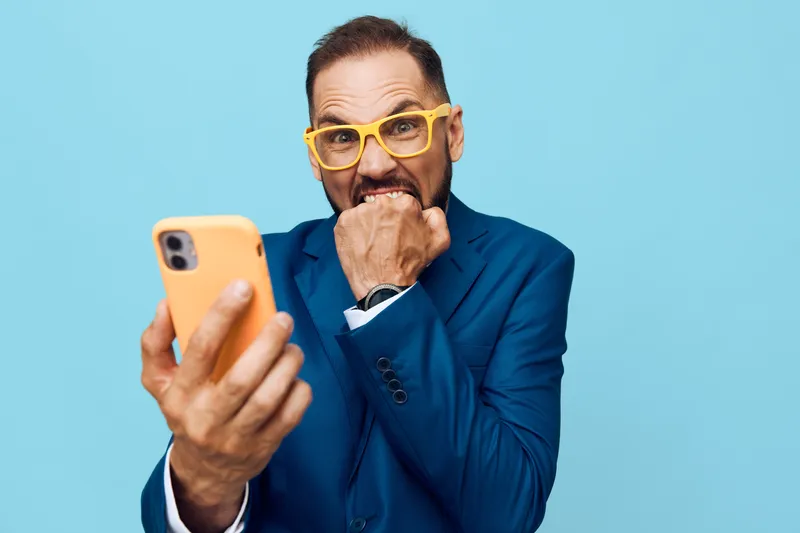A professional businessman on a vibrant colored backdrop checks his mobile with a tense, surprised expression, conveying urgency, focus, and emotion in a corporate setting.
