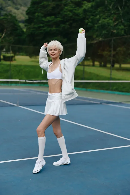 Energetic young athlete celebrating on a tennis court, dressed in white sportswear, exuding joy and confidence in a lush green environment