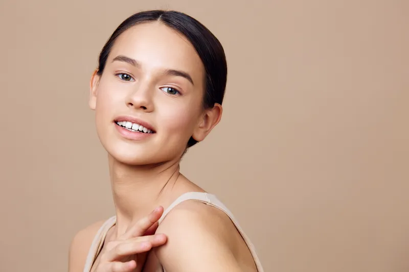 Smiling young model with clear skin and braces on a neutral beige background, showcasing natural beauty and confidence, ideal for beauty and skincare concepts