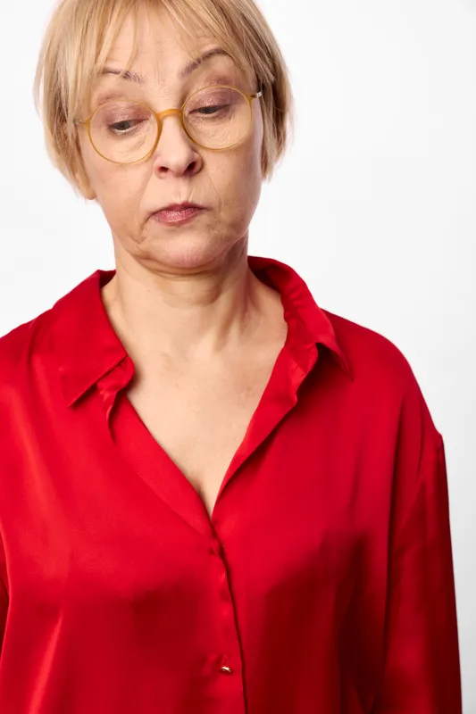 Woman with glasses and short hair, wearing a red blouse, closeup portrait on a white background, mature serious mood, neutral gaze, soft shadows, studio lighting, indoor fashion concept