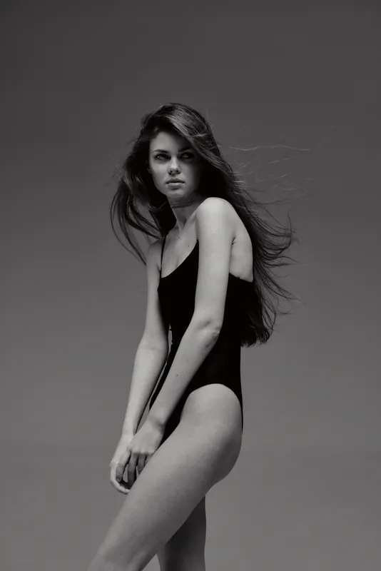 Black and white portrait of a young woman in a swimsuit with flowing hair and serious expression