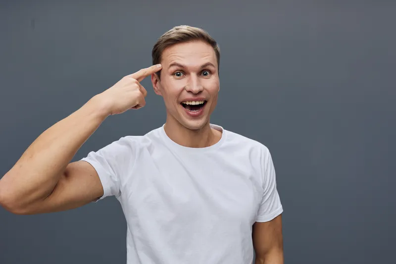 cheerful young man pointing head smiling wearing white t-shirt casual confident facial expression isolated on gray background digital detox concept