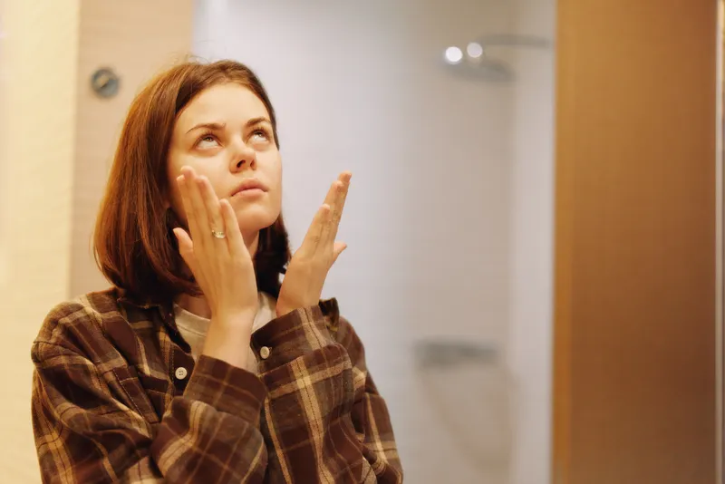 Woman in plaid shirt looks upwards with a thoughtful expression in an indoor setting, casual portrait capturing curiosity, self reflection, warm light, soft background, and everyday mood in a studio
