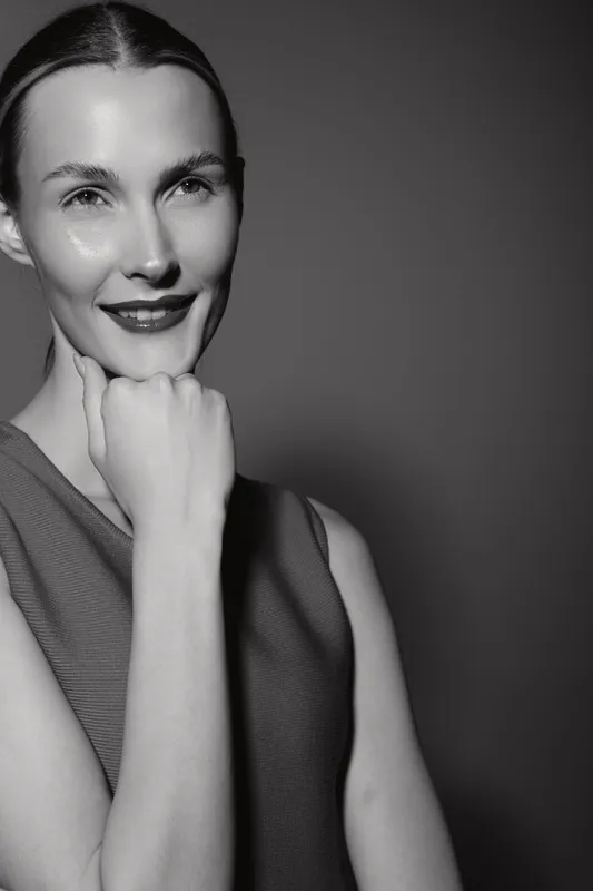 Smiling white woman with light skin and dark hair poses confidently in sleeveless top against plain background. Concept for beauty and portrait.