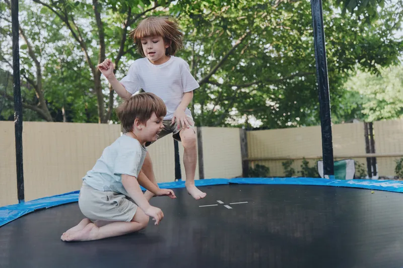 Joyful children jumping on a trampoline in a sunny backyard, enjoying their playful day filled with laughter and excitement outside in nature.