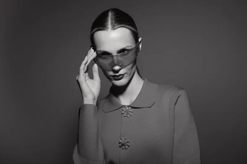 Elegant white woman with pale skin wears modern sunglasses and knitted dress with floral details. Fashion portrait in monochrome with confident and stylish mood.