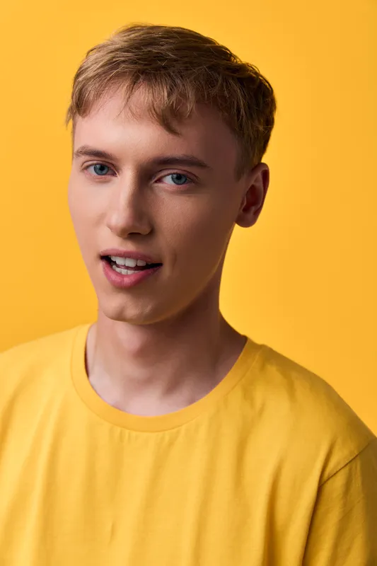 Young man, smiling, yellow shirt, bright background, studio lighting, casual fashion and confident expression for lifestyle, fashion, and photography usage in media projects